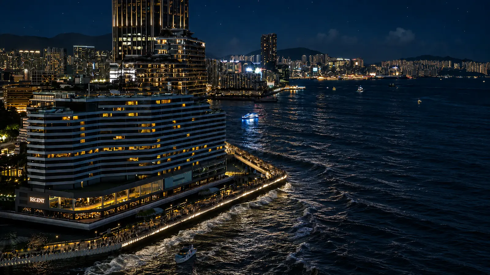 夜の維多利亞港。手前の岸に建物が並び、その灯が窓ごとに琥珀色に点っている。岸の縁を白い波頭が洗い、沖には対岸の街の灯が横一列に伸びる。空は青みの残る黒で、星がいくつか見える。